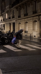 Elderly person crosses Paris street at night carrying shopping bag