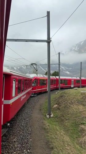 Red train spotted navigating Alpine landscape near Poschiavo, Switzerland