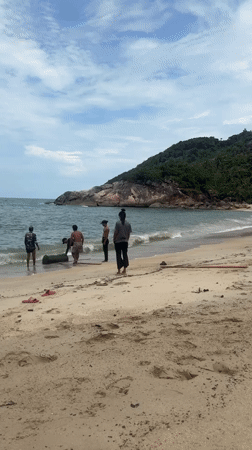 Group moves heavy barrel on Thai beach using planks