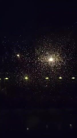 This video shows a dark outdoor scene with many small, bright, bokeh lights. These lights are scattered across the dark background, suggesting they are from distant sources such as streetlights or stars. The lights appear to be blurred and out of focus, which is a common effect in photography when the subject is not in focus or when there is a shallow depth of field. The overall impression is of a nighttime setting, possibly with rain or condensation on a window, which would further enhance the bokeh effect of the lights.
