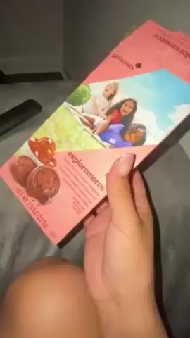 Here is a brief description of the video:
The video shows a person holding a box of Girl Scout cookies in a living room. The cookies are the "Exploremores" variety. The camera pans to a television that is playing a fantasy movie or television show. The TV is on a stand with a video game console and some other objects on it.