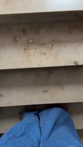 The video shows a person wearing blue jeans and sandals walking down a set of stairs. The stairs appear to be made of a light-colored material with some staining or discoloration. The perspective is from the person's point of view, looking down at their feet and the stairs ahead. The person is moving from a higher level to a lower level, indicated by the downward angle of the stairs.
