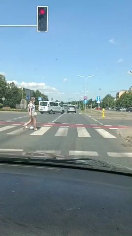 The video shows a view from a car at a pedestrian crossing with two women in it. The pedestrian signal is red, and the women are walking across the street. There are cars and buildings in the background. The weather is sunny and clear.