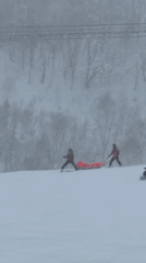 Skiers transport person on sled in Kutchan snow
