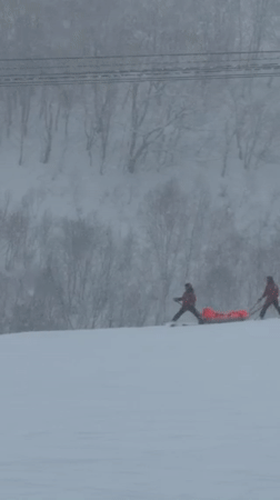 Skiers transport person on sled in Kutchan snow