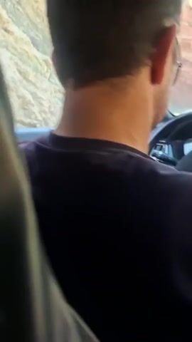 The video is a short clip taken from inside a moving vehicle. The camera is pointed out the window, capturing blurred views of the roadside. The landscape appears to be rocky and mountainous, with sparse vegetation. The sun is bright, causing glare on the window. The window itself is quite dirty, with dust and spots obscuring the view. There is no discernable presence of people or complex actions. The dominant elements are the motion of the car, the changing scenery outside, and the condition of the car window.