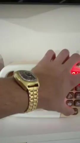 A person wearing a gold watch presses the start button on a toy microwave. The red LED lights inside the microwave come on. The microwave's timer counts down.