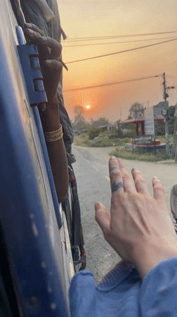 Passengers hang from moving blue vehicle in Nepal