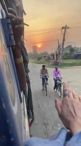 Passengers hang from moving blue vehicle in Nepal
