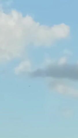 The video shows a bright, sunny sky with a few scattered clouds. High in the sky, there is a small dark object that could possibly be an airplane or a bird. The camera is pointed upwards and remains still.