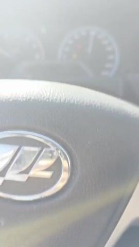 The video begins with a close-up of a car's steering wheel and dashboard, showing the speedometer indicating a speed of approximately 100 km/h. The view then shifts to a first-person perspective from the driver's seat, looking out through the windshield. The car is on a highway with clear skies and a few sparse clouds. The road is paved and appears to be in good condition, with white lane markings visible. There is a guardrail on the left side of the road and a grassy embankment on the right. Streetlights are visible along the side of the highway. The car is traveling at a steady speed, and other vehicles are not clearly visible in the frame. The overall impression is that of a smooth and uneventful drive on a highway during the daytime.