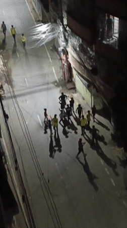 Nighttime street gathering in Dhaka with yellow-and-green flags