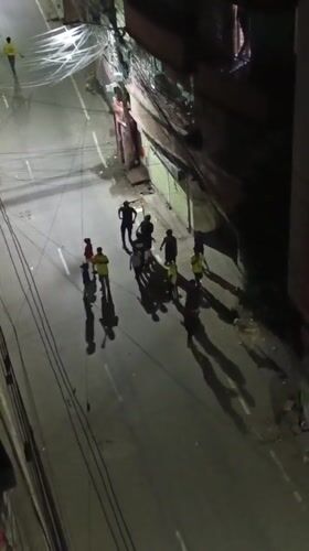 Nighttime street gathering in Dhaka with yellow-and-green flags