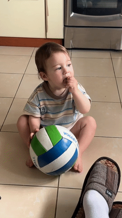 Toddler plays with a volleyball and Crocs on a tiled floor