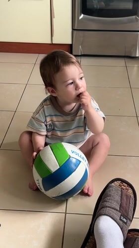 Toddler plays with a volleyball and Crocs on a tiled floor