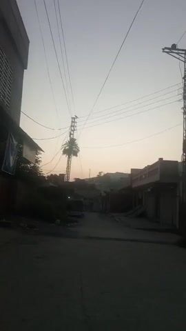 A street scene with buildings on either side and power lines overhead. The sky appears to be dusk or dawn. The camera is still.
