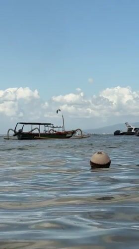 Lazy Bali beach morning with boats, beer, and kite surfers