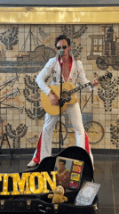 Elvis impersonator performs in white jumpsuit with acoustic guitar