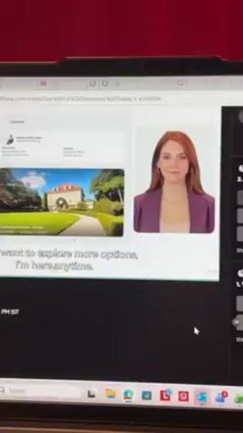 The video shows a person looking at a laptop screen. On the screen is a video conference call featuring a presentation by NVIDIA showcasing an avatar or digital human named Sophia. A woman appears in the main part of the screen as if she were speaking directly to the audience, and the text “Start a real-time conversation with Sophia. It’s the best demo I’ve seen from an avatar or digital human perspective.” appears. On the right-hand side of the screen are numerous small boxes, each containing the face of a participant in the video conference. The video is being watched on a laptop which is sitting on a desk against a red wall. The time 5:55 PM-8:00 PM IST is visible.