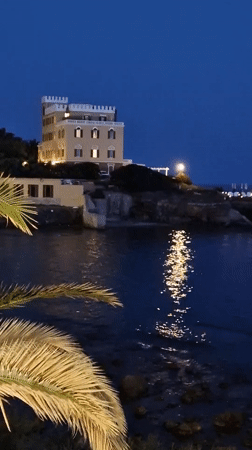 Crenellated building on Alghero's rocky coast at dusk