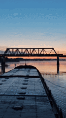 Barge approaches railroad bridge at sunset in Нифантово, Russia