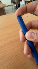 Person clicks blue pen at wooden desk