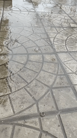 Rain pools ripple across patterned pavement in Hîrjău