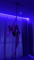 Woman practices pole dance in blue-lit studio