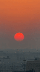 Red sun over a hazy city skyline at golden hour