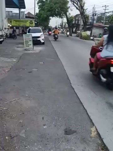 A group of people on motorcycles are riding down a street in a suburban area. The street is paved and lined with trees and buildings. The sky is overcast. The time of day appears to be late afternoon or early evening.