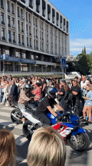 Motorcyclists gather near bank; woman takes selfie in Saint-Tropez