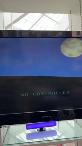 The video displays a television screen showing a video game screen with the text NO CONTROLLER. The game depicts a silhouette of a rider on a horse galloping across a hill under a large moon in a nighttime sky. The television is an Emerson brand. Below the screen, a purple LED light bar is visible, reflecting on a glass surface. The background appears to be an indoor setting with a white ceiling structure.