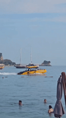 Sunny beach day with boats, swimmers, and a busy waterfront