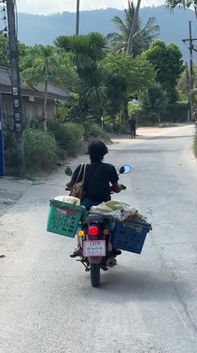 Motorcyclist travels narrow road in Baan Lamai, Thailand