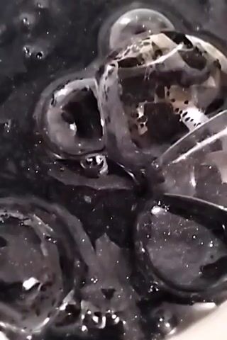A close-up shot displays a viscous, black liquid interspersed with clear, gelatinous spheres. The liquid appears to swirl around the spheres, creating a marbled effect. There are glints of light reflecting off the surface of the liquid and the spheres. The camera remains stationary, maintaining a tight focus on the liquid and spheres.