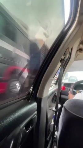 A video shot from inside a car shows a train passing by very close. The driver's hands are visible on the steering wheel. After the train passes, the landscape outside the window comes into view, revealing buildings and trees. The interior of the car is also visible.