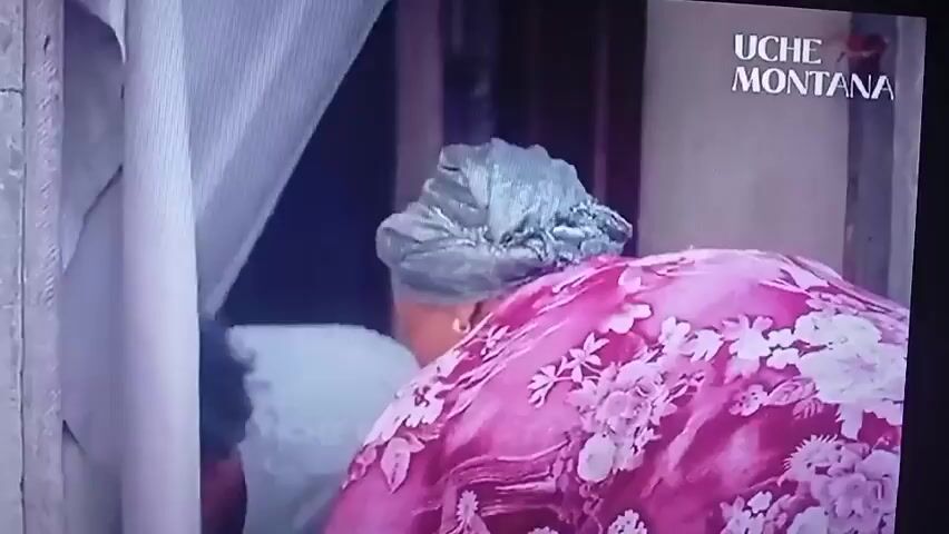 This video begins with a close-up of two individuals, one wearing a pink and white floral patterned garment and a light blue headscarf, kneeling over another person whose face is obscured. The first individual appears to be speaking to the person on the ground, saying "Daddy Monica stand up" and "Why are you doing this to me." The scene then transitions to an aerial view of a bustling city street, featuring tall buildings, a large church, and numerous cars and buses. The text "UCHE MONTANA" is visible in the top right corner of the screen.