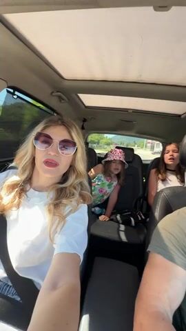 A car is driven with people inside. A woman is in the driver's seat, a small girl is in the back left seat, and another girl is in the back right seat. A male passenger is in the front right seat. The car has a sunroof.