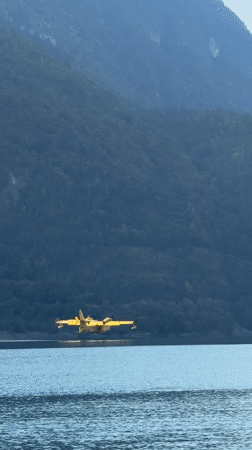 Yellow seaplane skims Lake Molveno on a clear Alpine morning