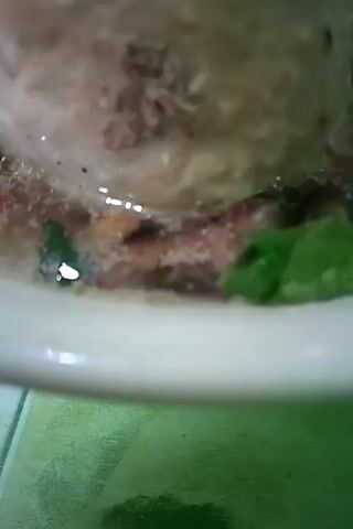 The video shows a close-up of a bowl of soup with large meatballs and some greens. The soup appears to be broth-based with noodles and other small ingredients. The meatballs are round and a light brown color. The greens are dark green and leafy. The bowl is white. The camera is held at an angle, looking down into the bowl. The lighting is dim.